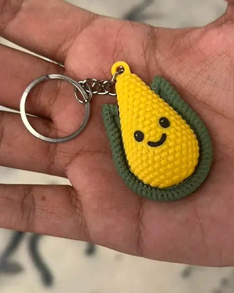 Llavero de elote amarillo con carita sonriente y hojas verdes.